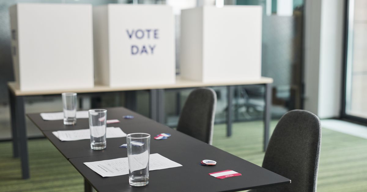 A prepared voting station with tables, chairs, and privacy booths in a conference room.